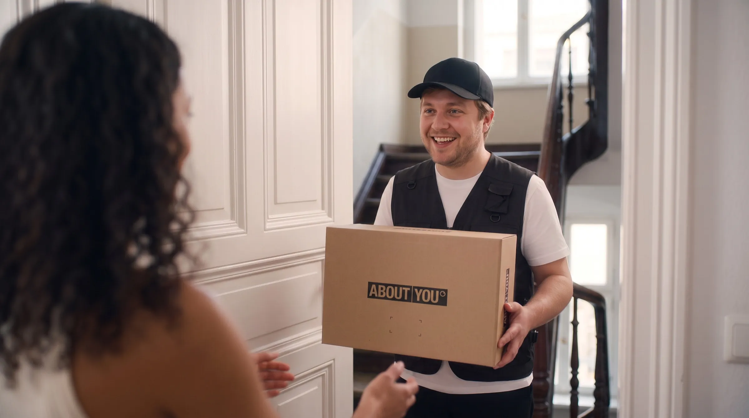 KI-Werbespot ABOUT YOU x Google: lächelnder Paketbote mit einem ABOUT-YOU-Paket an der Tür